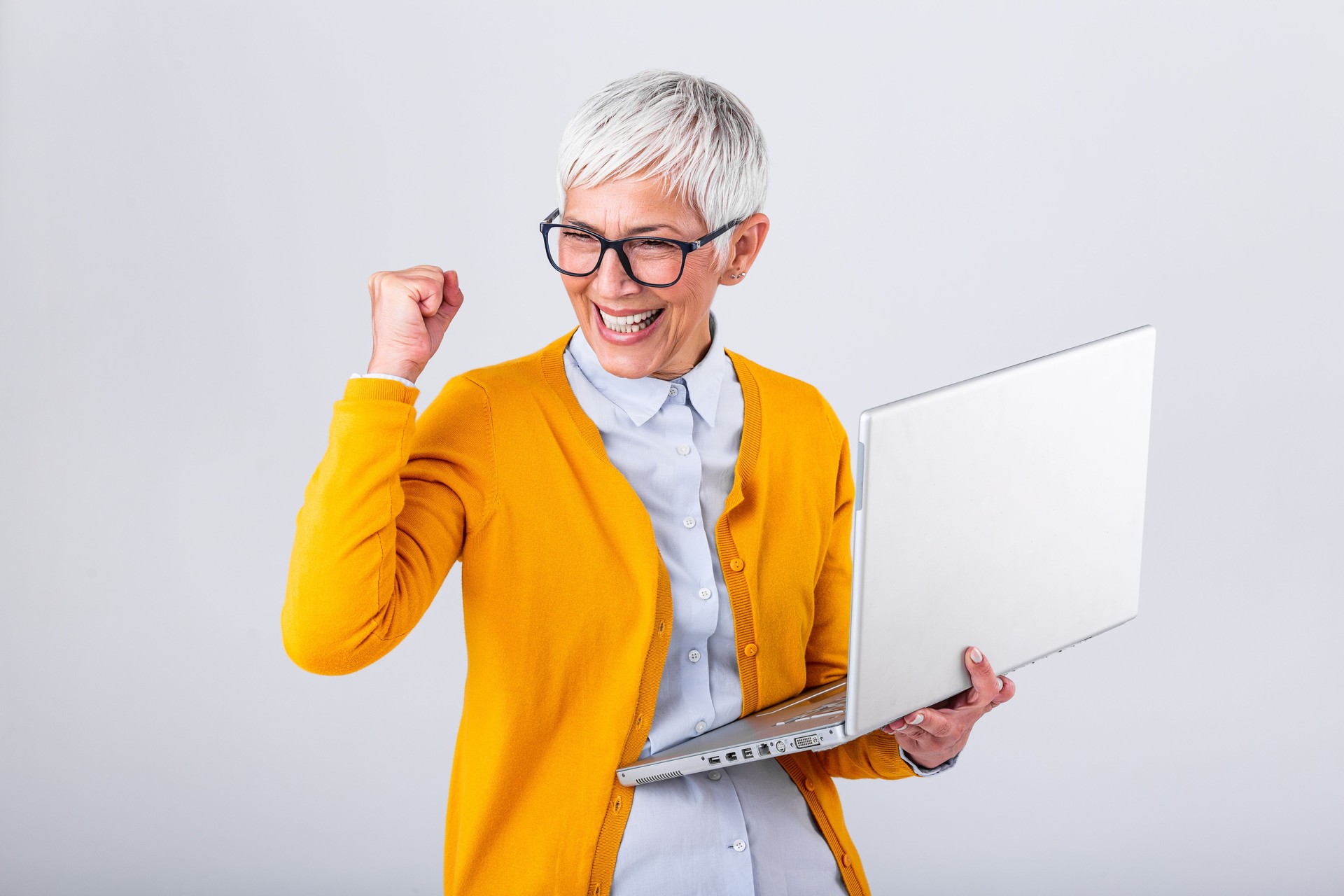 Portrait of a cheerful mature woman with a laptop computer and celebrating success isolated over gray background. Senior lady watching celebrating online bid bet win or great result victory concept